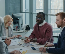 Four professionals sit around a table in a modern office, discussing documents and using laptops during a business meeting focused on business risk and mitigation.
