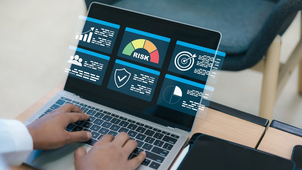 Person using a laptop displaying digital dashboards with charts, graphs, a risk meter, shield icon, target, and user icons, indicating data analysis and cyber risk assessment activities.