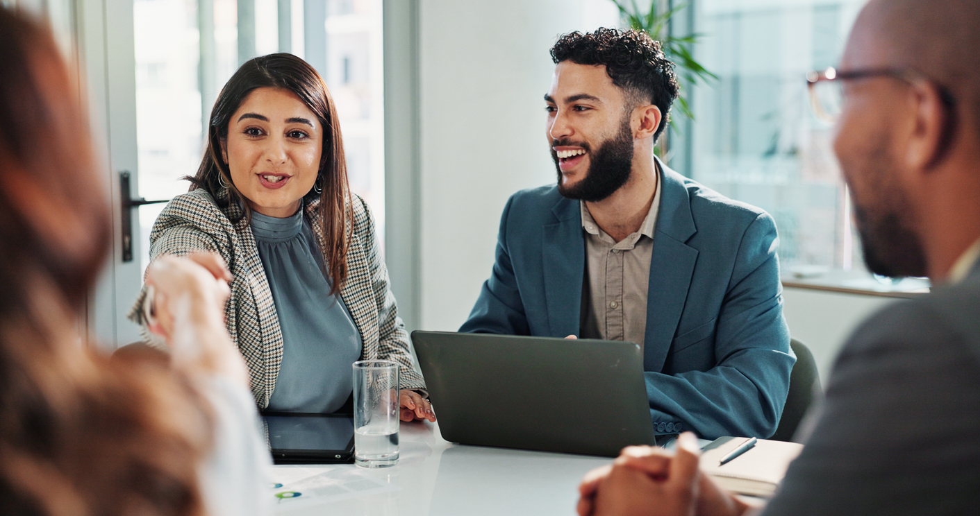 Two business professionals smile and shake hands across a conference table.
