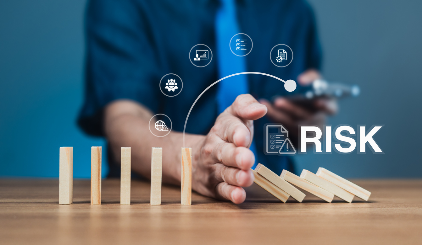 A hand stops a row of falling wooden blocks with digital risk-management icons above.