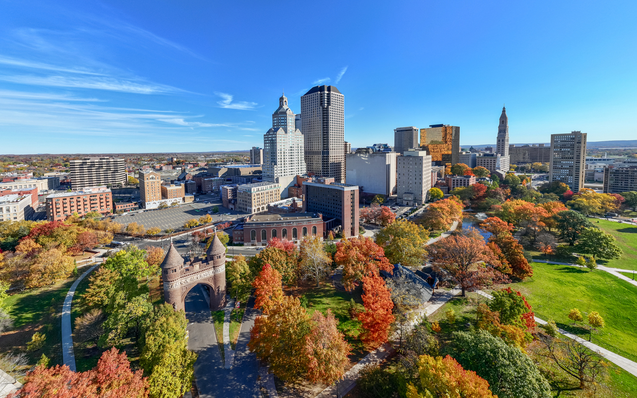 Hartford, Connecticut skyline above a park with autumn trees and an arched gate.